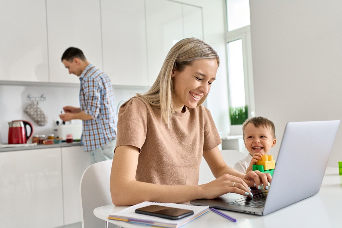 mamma felice che lavora a casa usando il laptop mentre il figlio divertente del bambino gioca.