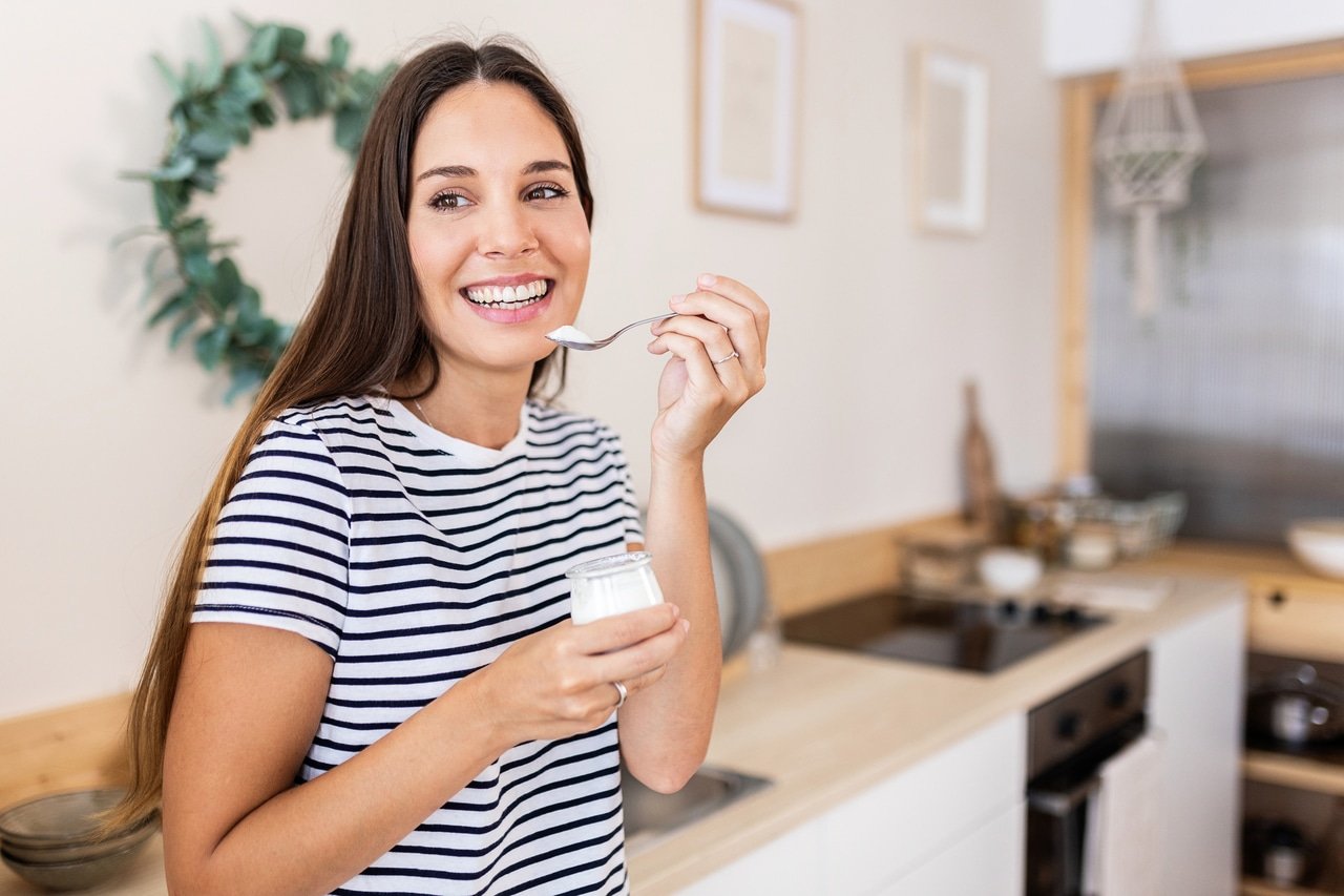 giovane donna adulta serena che fa colazione a casa mangiando yogurt bio bianco